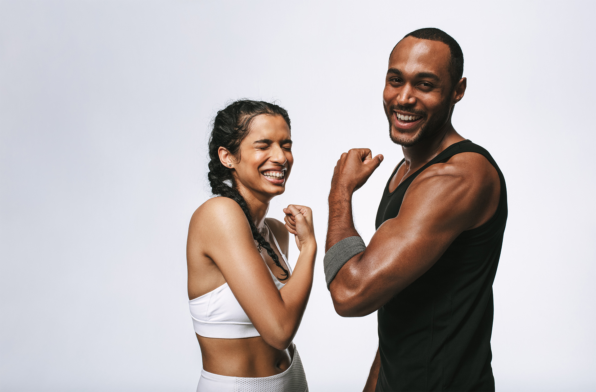 Couple athlétique souriant, homme et femme en tenue sportive, montrant leurs biceps. Photo joyeuse symbolisant la motivation et le bien-être sur Joyful Body.